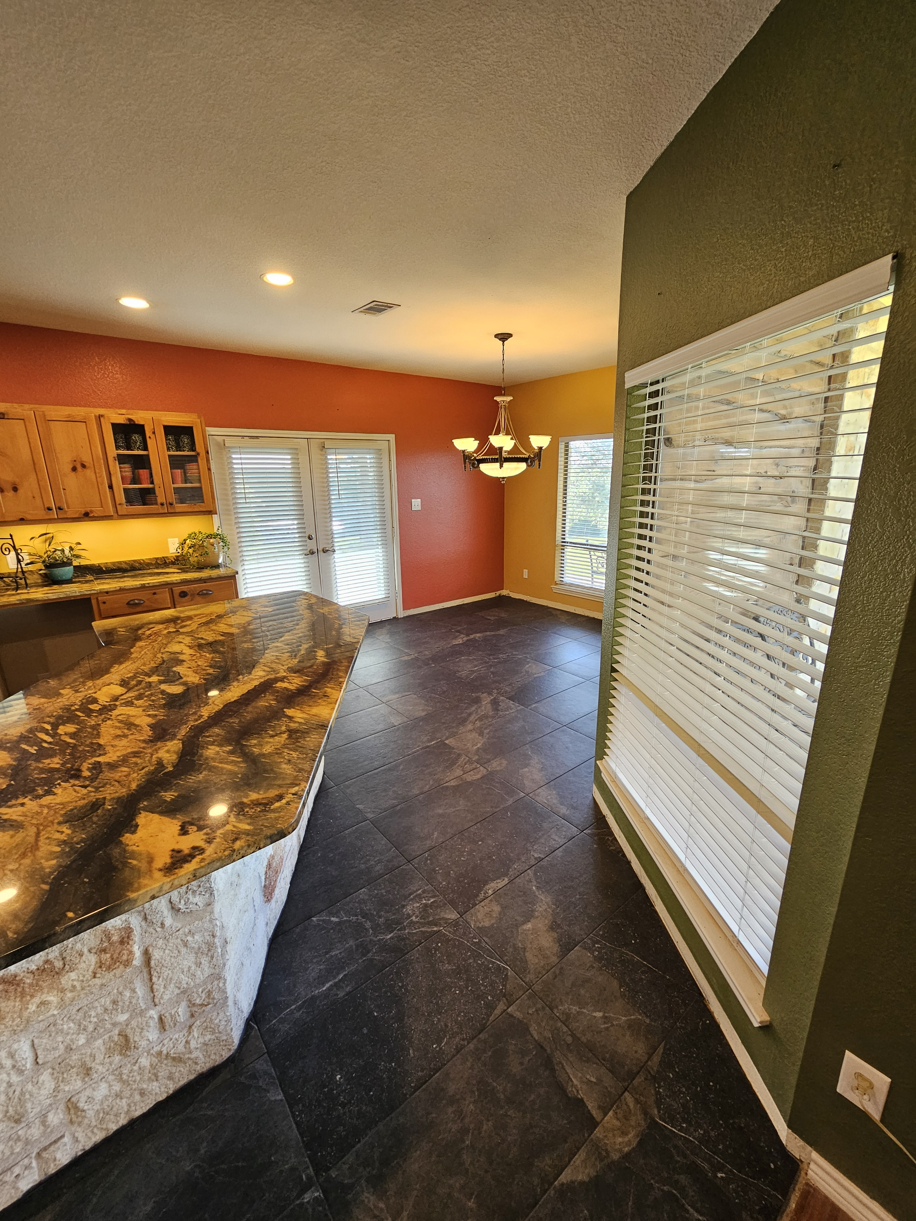 Dark large-format kitchen floor tile extending toward windows and a kitchen island.