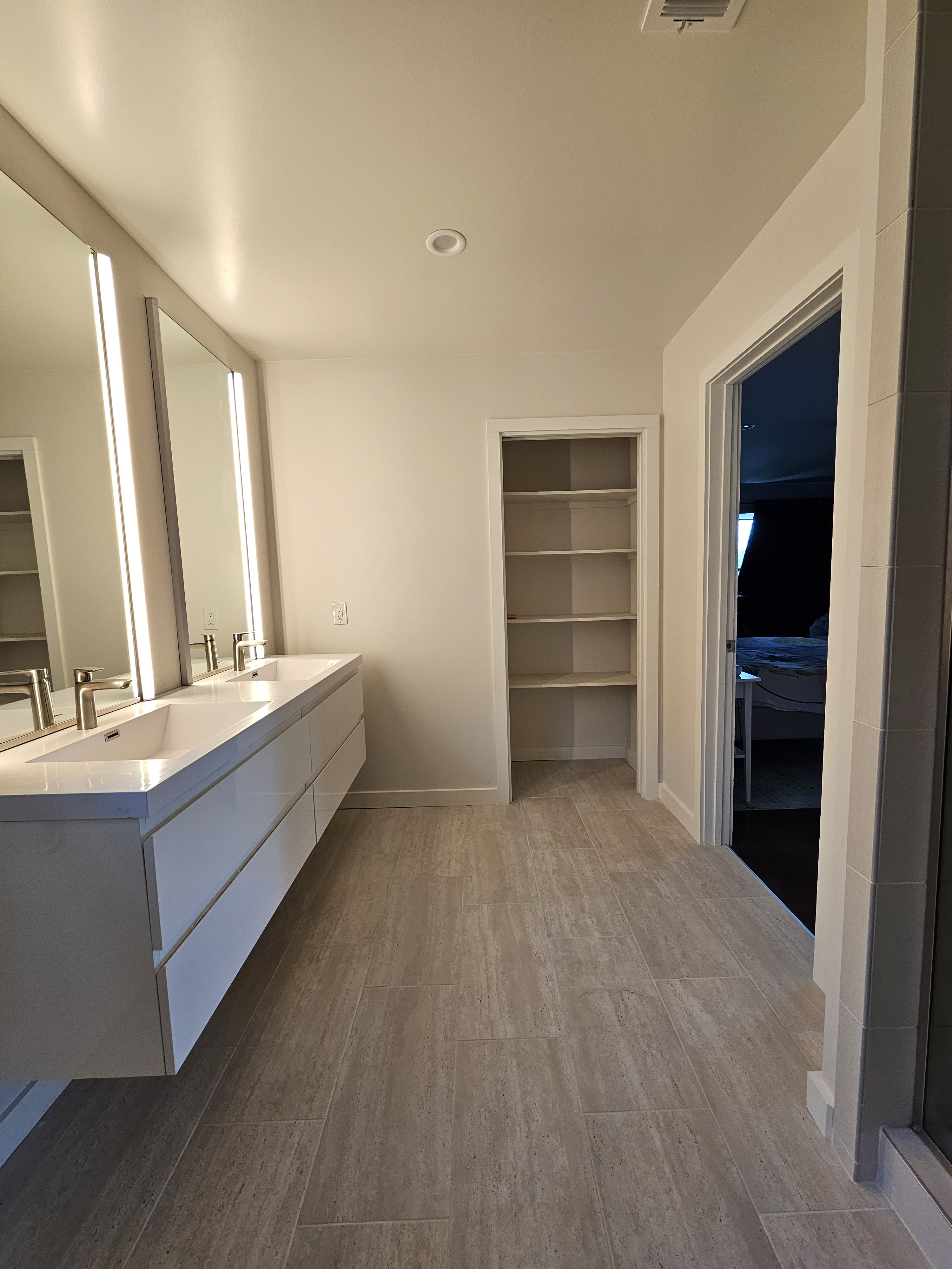 Long view of light bathroom floor tile with a vanity and built-in shelving.